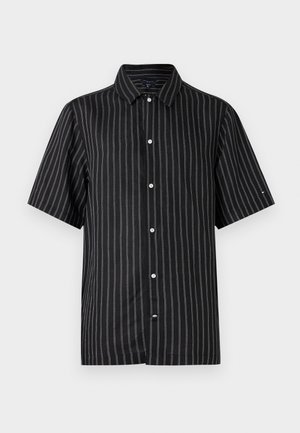 Chemise noire à manches courtes, boutonnée, avec des fines rayures verticales blanches et un col classique, disposée à plat sur un fond blanc.