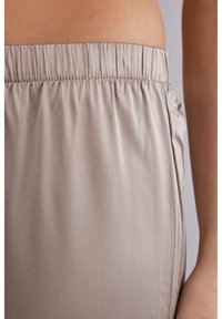 Lichtbeige broek met elastische tailleband van glad, glanzend materiaal. Voorzien van zijnaaddetails en een ontspannen pasvorm. Zachte textuur en casual ontwerp.