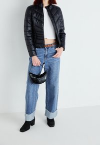 Zwarte pufferjack met chevron-quilting, gecombineerd met lichtblauwe wijde jeans. Zwarte haklaarzen en een kleine zwart gestructureerde handtas.