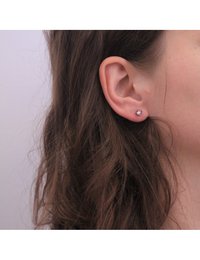Boucles d'oreilles en argent métallique avec des pierres précieuses roses rondes, fixées au lobe de l'oreille, affichant un design lisse et minimaliste.