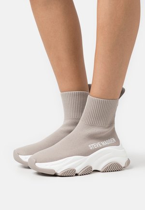 Sokstijl sneakers in licht beige met een gestructureerde afwerking en een geribbelde boord. Voorzien van een dikke witte zool met een golvend patroon en subtiele branding.