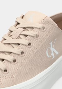 Μπεζ πάνινο αθλητικό παπούτσι με στρογγυλά κορδόνια, απαλές ροζ τρύπες, λευκή ελαστική σόλα και ανάγλυφο λογότυπο. Υφασμάτινη επιφάνεια με ραφές λεπτομέρειες.