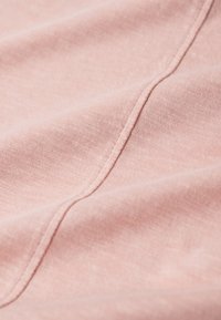 Jasnoróżowy materiał o miękkiej fakturze, z widocznym ściegiem na krawędziach w dopasowanym kolorze nici.