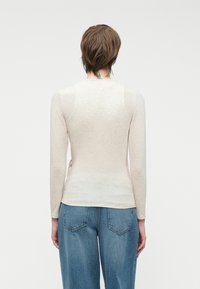 Vaaleanbeige pitkähihaine paita, joka on valmistettu ohuesta, tekstuurilla varustetusta kankaasta, pyöreä kaula-aukko ja istuva malli. Yhdistetty sinisiin korkeavyötäröisiin farkkuihin.