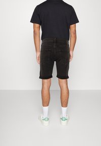 Svarta denimshorts med upprullade fållar, en figursydd design och två bakfickor. Matchas med en svart t-shirt och vita sneakers med gröna detaljer.