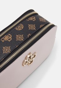 Růžová kožená taška s černým vzorovaným zipem. Zlaté kovové doplňky a zipy, zaoblený tvar, s dekoračním logem.