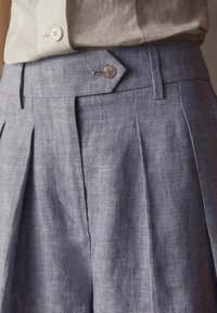 Ljust blå linneshorts med frontveck, knappstängning och slät textur, med skräddarsydd midjeband och diskreta sömdetaljer.