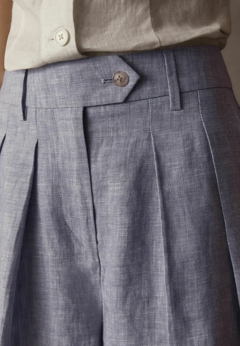 Ljust blå linneshorts med frontveck, knappstängning och slät textur, med skräddarsydd midjeband och diskreta sömdetaljer.