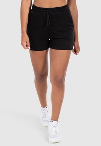 Shorts en coton noirs avec une taille élastique et un cordon de serrage. Présente un détail de logo discret sur l'ourlet. Associés à des baskets blanches.