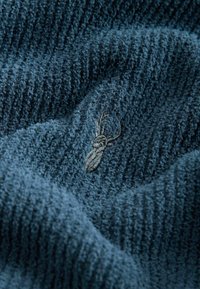 Dunkelblaues strukturiertes Gewebe mit einem wellenförmigen Muster und einem in Grau gestickten Spinnendesign. Weiches und plüschiges Material.