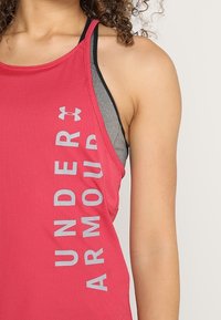 Rosa sportliches Tanktop mit gerippter Struktur, versehen mit einem grauen Logo und einem vertikal an der Seite verlaufenden Schriftzug. Dünne Träger und mehrlagiges Design.