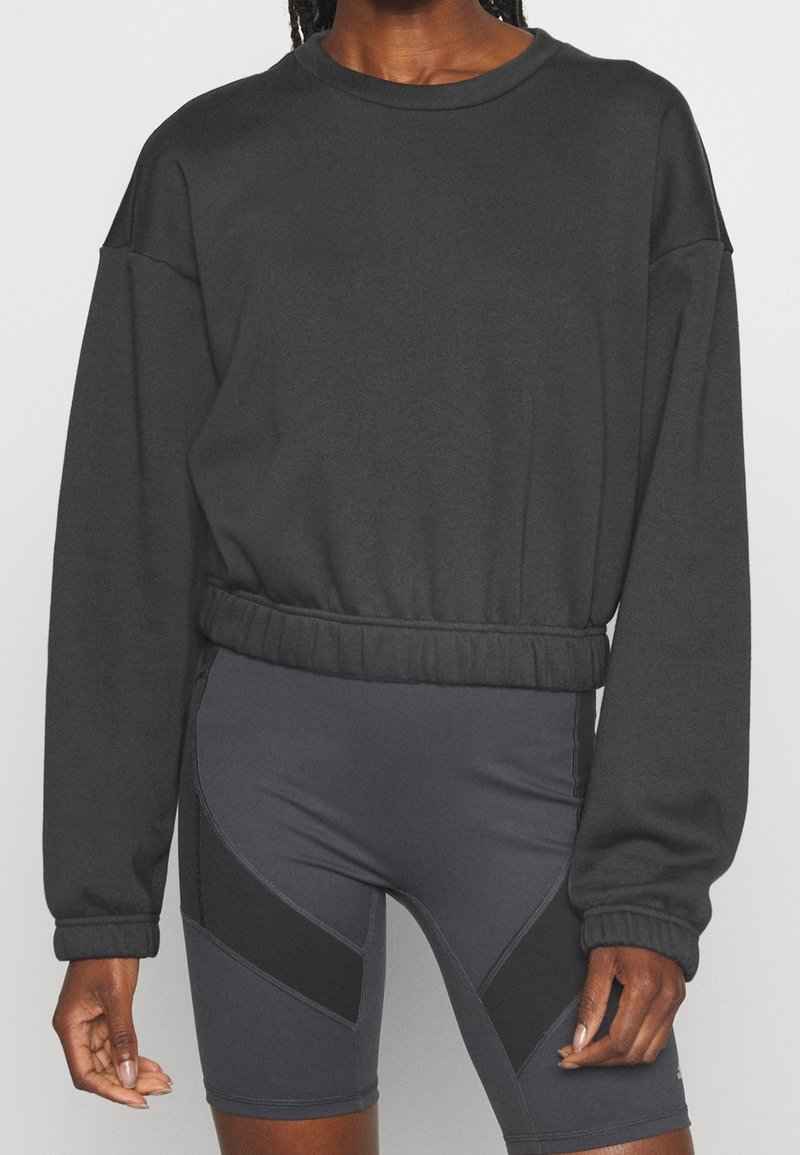 Personne portant un sweat-shirt court à manches longues noir avec un ourlet élastique et un short de cyclisme taille haute gris foncé avec des panneaux noirs.