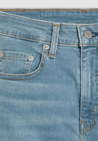 Vaqueros de denim azul claro con una textura desgastada, que cuentan con un bolsillo frontal, costuras de cobre y botones de hardware metálico.