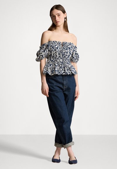 Ziedu topiņš ar atvērtām plecu daļām un pūkām piedurknēm tumši zilā krāsā, ar baltām ziedu rakstām un smockētu vidukli, pārī ar sarullētām tumšām džinsām.