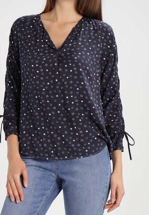 Blouse marine avec motif d'étoiles blanches et bleues, en V, manches trois-quarts avec liens aux poignets, fabriquée en tissu léger.
