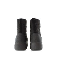 Botines negros con parte superior de cuero suave y tela, punta redonda, detalles texturizados en el tacón y suela de goma plana.