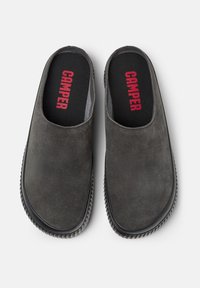 Zuecos de ante gris con una superficie texturizada, diseño deslizante y suelas de goma negra. En el interior cuentan con una plantilla acolchada con "CAMPER" en rojo.