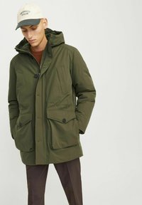 Parka acolchada de color verde oliva con capucha, dos bolsillos frontales con solapa y cierres de botón. Tejido texturizado con un acabado suave.
