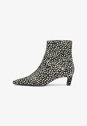 Zwarte enkelboot met witte onregelmatige stippen, puntige neus, lage kittenhak en klein gouden logo nabij de bovenrand.