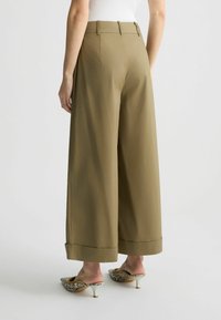 Pantaloni a gamba larga in tessuto verde oliva, con vita alta sartoriale, cuciture precise e orlo ripiegato. Abbinati a mule a punta stampate.