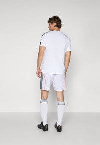 Hvid atletisk trøje og shorts med sorte striber og orange detaljer. Sorte fodboldstøvler og knælange hvide sokker med sorte striber.