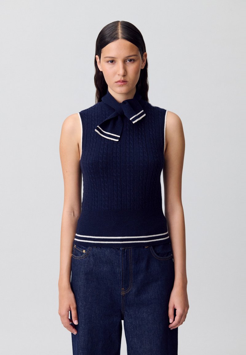 Top sin mangas de punto azul marino con un escote con lazo, que presenta detalles a rayas blancas en el cuello y el dobladillo. Tejido suave y texturizado.