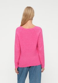 Różowy sweter dzianinowy z szerokim dekoltem, prążkowaną strukturą i długimi rękawami. Posiada zwężający się krój oraz boczne rozcięcia na dole.