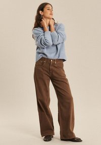 Jasnoniebieski, oversize sweter z ribbowymi mankietami, zestawiony z brązowymi spodniami o szerokich nogawkach, z przednimi kieszeniami i luźnym krojem.