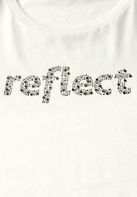 Bílý tričko s nápisem "reflect" vyrobeným z černých rhinstonů, s oválným výstřihem a měkkou, žebrovanou texturou.