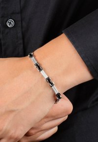 Bracciale da polso in argento e nero con anelli intrecciati, caratterizzato da una sezione in rete texturizzata. Finitura liscia e colori a contrasto.