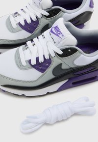 Bijele Nike Air Max tenisice imaju kombinaciju sivih i ljubičastih akcenta, teksturiranih panela i istaknuti crni swoosh. Uključuju bijele vezice.