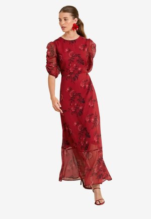 Czerwona maxi sukienka w kwiaty z przezroczystymi puff sleeves, dopasowanym topem i zwiewnym dołem. Posiada wzór róż i podkreśloną talię.
