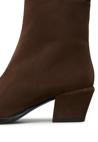Stivale alla caviglia in suede marrone con finitura testurizzata, caratterizzato da un tacco ampio e angolato e una silhouette affusolata e slanciata.