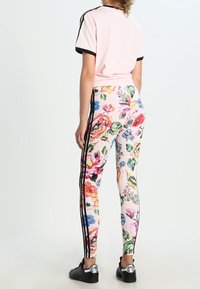 Blommiga leggings med vit bakgrund, som har färgglada blommor och svarta sidostreck; kombinerat med en rosa kortärmad topp.