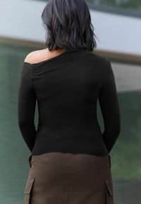 Melnā off-shoulder garajaka ar garām piedurknēm, izgatavota no mīksta auduma, kombinēta ar brūnu svārku ar sānu kabatām un elegantu, piegriezuma dizainu.