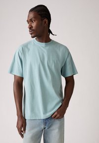 Lyseblå bomulds T-shirt med rund hals og korte ærmer. Har et lille, diskret broderet logo på brystet. Bæres med lyse denim jeans.