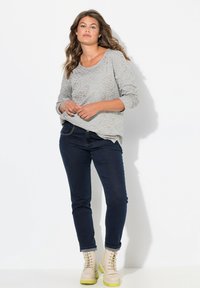 Ljusgrå, texturerad långärmad topp i kombination med mörkblå jeans. Beiga snörstövlar med en grön sula kompletterar outfiten.