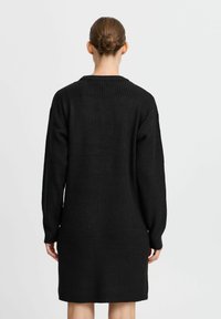 Svart stickad klänning med ribbat mönster, långa ärmar och rundad halsringning, som faller strax ovanför knäet, med minimalistiska detaljer.
