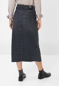 Mørk denimnederdel med lige snit, rå kant og baglommer. Båret med sorte loafers og grå sokker. Har en mærket talje.