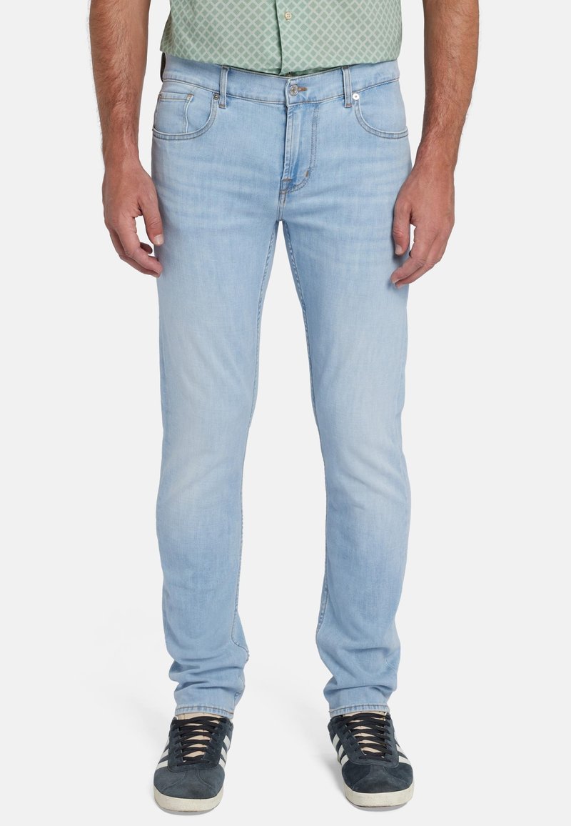 Jeans in denim azzurro chiaro, slim fit, cinque tasche, leggera scoloritura, dettagli cuciti, chiusura con bottone e cerniera, indossati con sneakers blu navy.