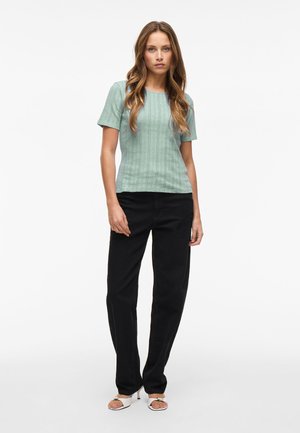 Lys grøn short-sleeve topp med vertikal ribbet tekstur, parret med løse sorte bukser. Modell som har på seg hvite sandalletter med åpen tå.