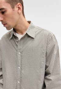 Light gray checkered button-up shirt made of soft fabric, featuring a single chest pocket and a structured collar.