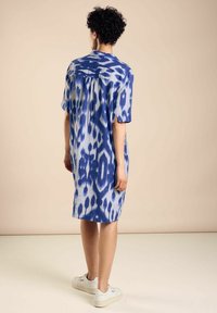 Niebieska i biała sukienka koszulowa w wzory, z krótkimi rękawami, luźnym krojem i detalem w postaci zakładki z tyłu. Gładki materiał, długość do kolan, zestawiona z białymi trampkami.