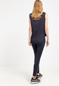 Námořnický bezrukávový top s asymetrickým zakončením, doplněný o slim fit námořnické kalhoty se bočním zipem a strukturované černé tenisky.