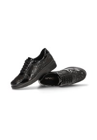 Zapatos casuales de charol negro con textura estampada y bandas elásticas, mostrados desde ángulos lateral y superior sobre fondo blanco.