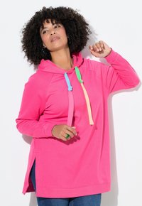 Růžová mikina s kapucí, klokáním kapsou, barevnými šňůrkami a bočními rozparky. Vyrobena z měkké látky s volným střihem a dlouhými rukávy.