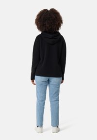Felpa nera con cappuccio dalla vestibilità rilassata, tessuto testurizzato e tasca a marsupio, abbinata a jeans blu chiaro a gamba dritta e sneakers bianche.
