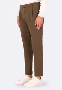 Pantaloni marroni a sigaretta con pieghe, dotati di una texture liscia e cintura elastica. Abbinati a sneakers bianche low-top.