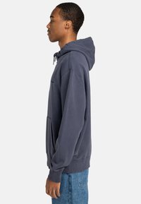 Sudadera de color azul marino hecha de algodón, con un bolsillo tipo canguro, capucha con cordón y puños acanalados. Textura suave y corte relajado.