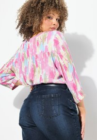 Kevyt, monivärinen pusero, jossa on siveltimen jälki -kuvio; 3/4 hiukset. Yhdistetty tummansiniset, istuvat farkut, joissa on takataskut.